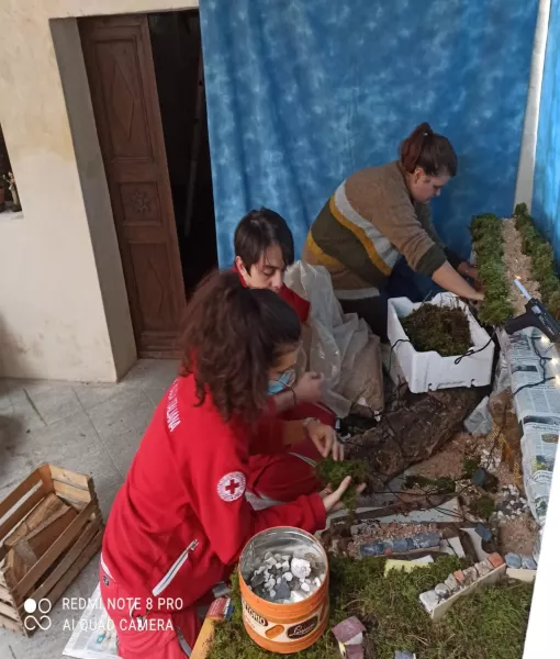 Tre giovani volontari della Cri Busca stanno allestendo il presepe di fronte alla cappella di San Giacomo