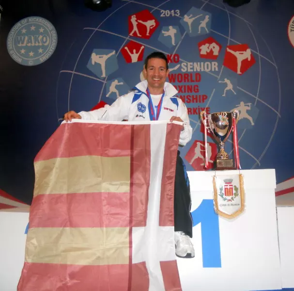 Bruno Manca sul podio con la medaglia d'oro mondiale per la categoria -63kg veteran di point fighting e con la bandiera e il gagliardetto della Città di Busca