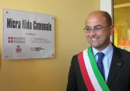 Il sindaco, Luca Gosso,  di fianco alla targa con i nomi degli enti che hanno contribuito alla costruzione del micronido: l'Asilo infantile di Busca, la Fondazione Crc, la Regione Piemonte, il Comune di Busca